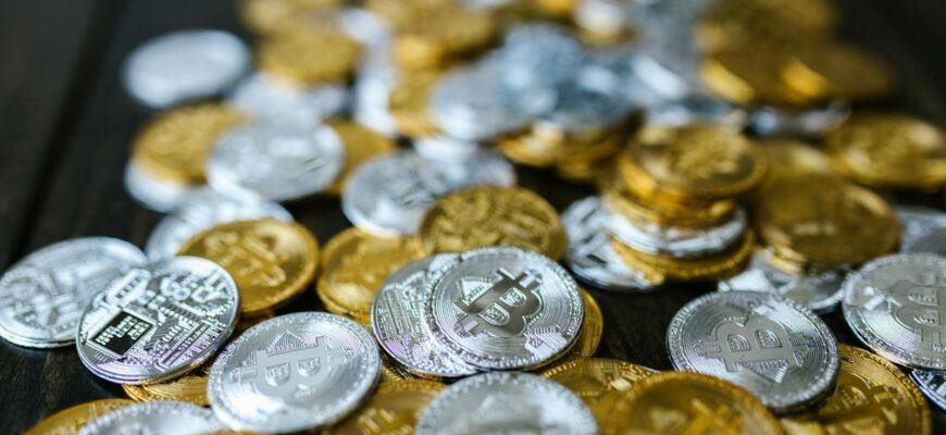 A collection of gold and silver cryptocurrency coins including Bitcoin and Ethereum on a dark surface.