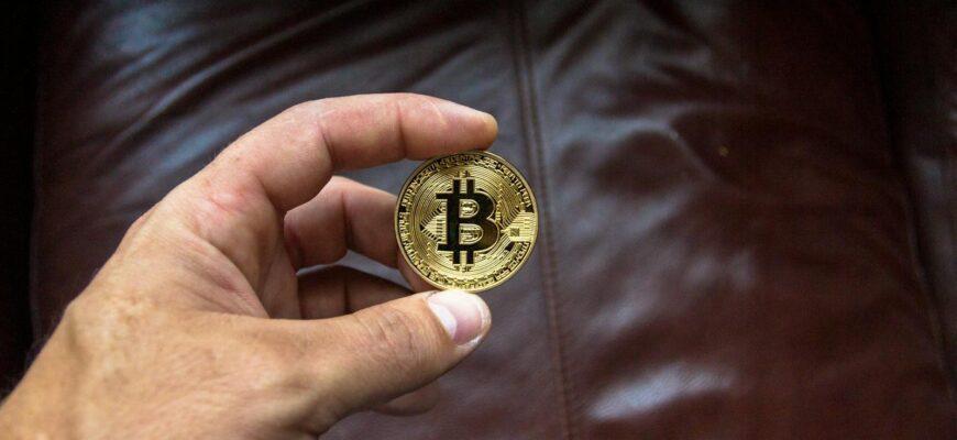 Close-up of a hand holding a gold Bitcoin cryptocurrency coin on a leather background.